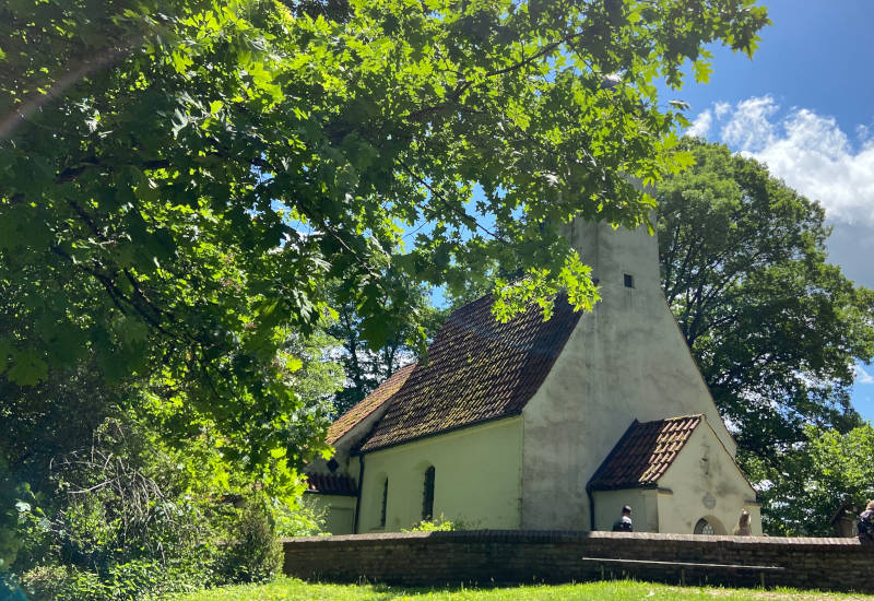 Kleine Kirche umgeben von Bäumen und grünem Gras.