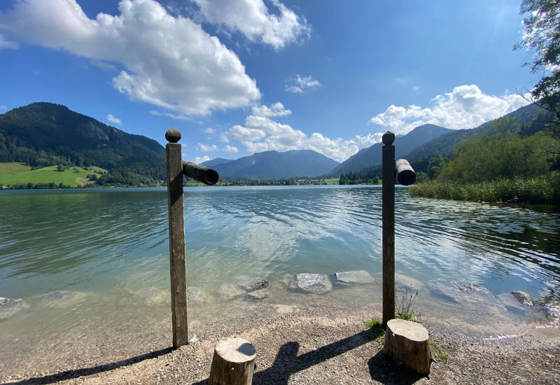 Holzfernrohre am Ufer eines Sees mit Bergen im Hintergrund