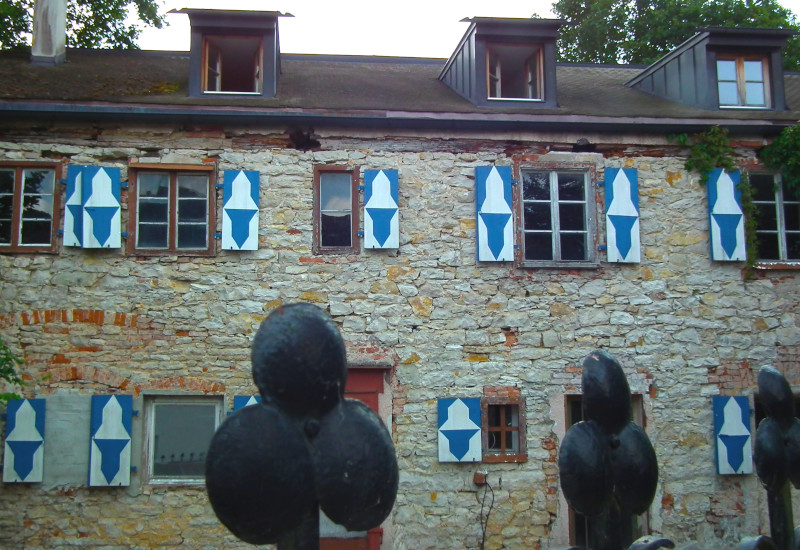 Steinmauer mit blauen Fensterläden und Eisenzaun.