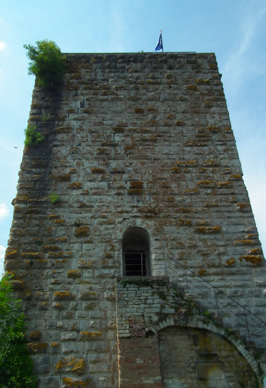 Hoher, steinerner Turm mit Fenster und Fahne oben.