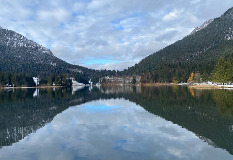 Bergsee mit spiegelndem Wasser und bewaldeten Ufern.