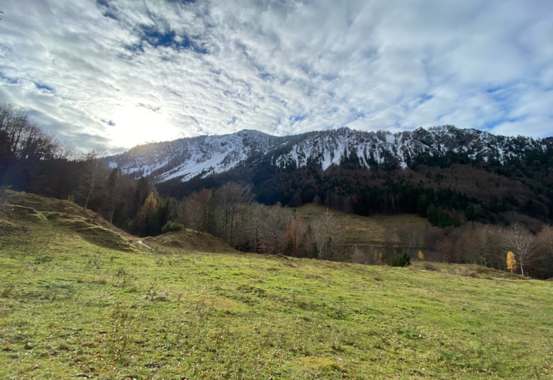 Berglandschaft mit Schnee, Wolken und grüner Wiese.