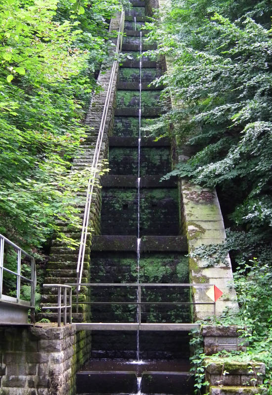 Wasserfall mit steinernen Stufen, umgeben von Bäumen.