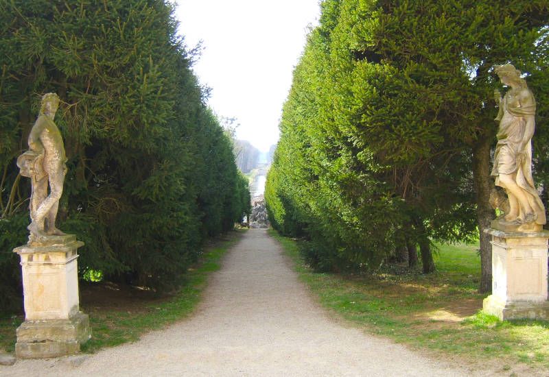 Allee mit Statuen und hohen Bäumen auf beiden Seiten.