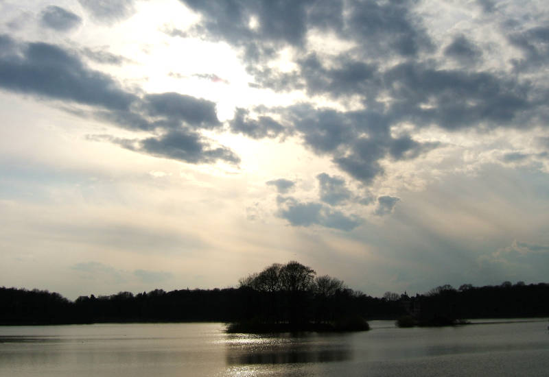 Sonnenstrahlen brechen durch Wolken über einem ruhigen See.