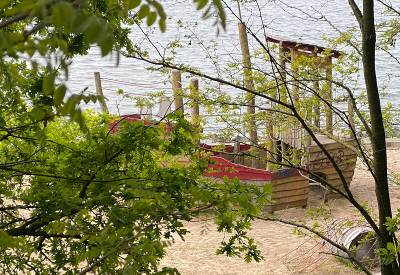 Spielplatz am Wasser, umgeben von Bäumen und Sträuchern.