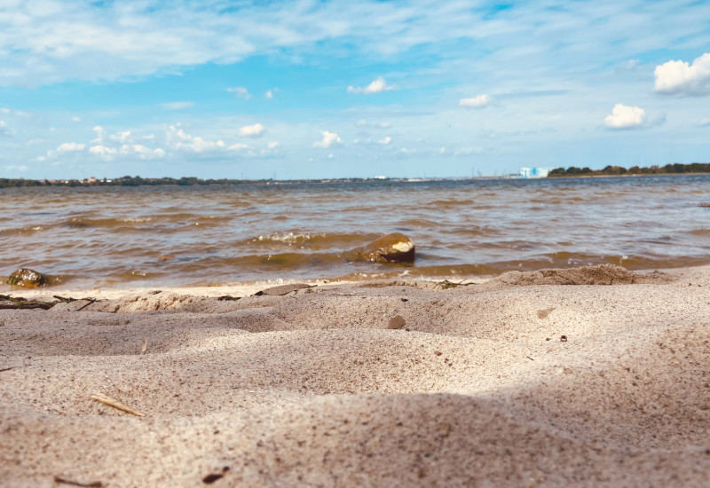 Sandstrand mit Wasser und blauem Himmel im Hintergrund.