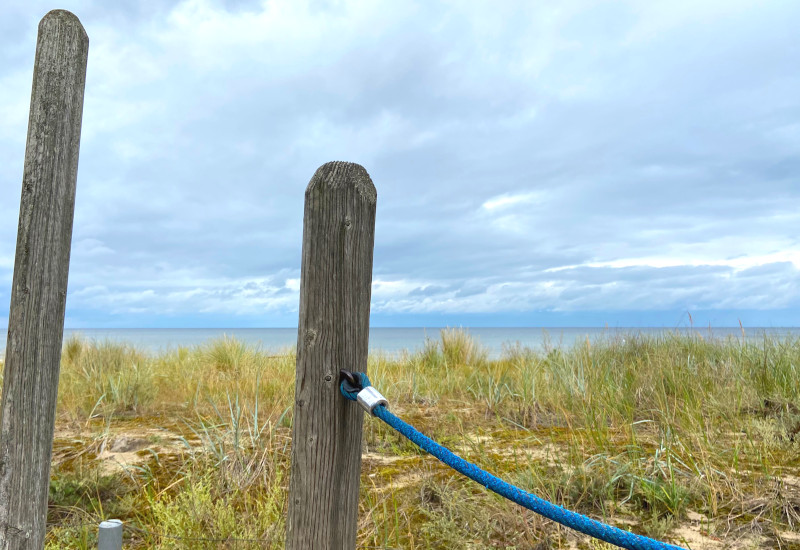 Holzpfeiler mit blauer Schnur, im Hintergrund Meer und Gras.