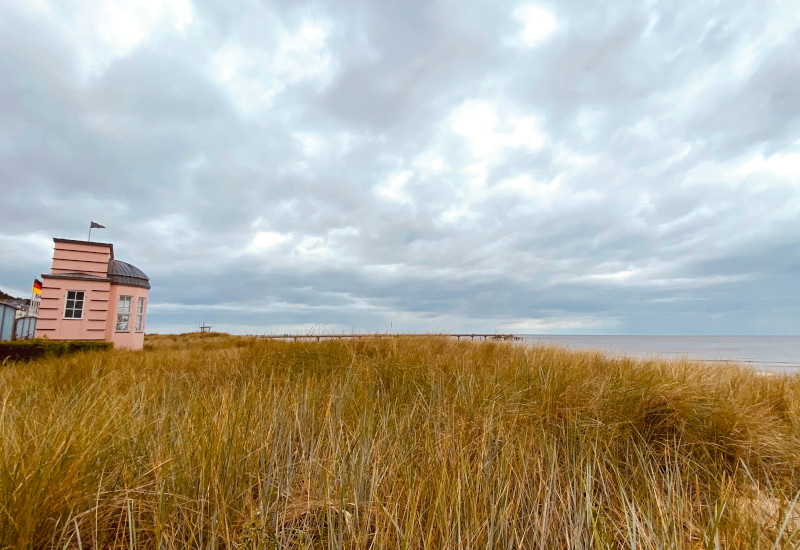 Rosa Gebäude am Strand mit Gras und bewölktem Himmel.