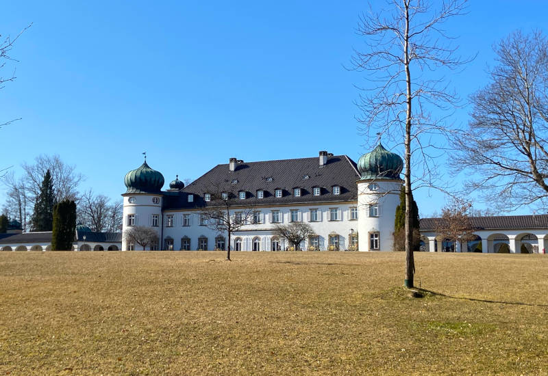 Schloss mit grünen Kuppeln vor blauem Himmel und Wiese.