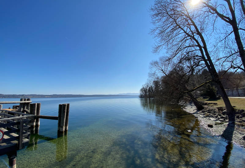 Ruhiger See mit Holzsteg und Bäumen im Hintergrund.