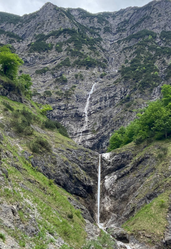 Berglandschaft mit Wasserfall und grünen Bäumen.