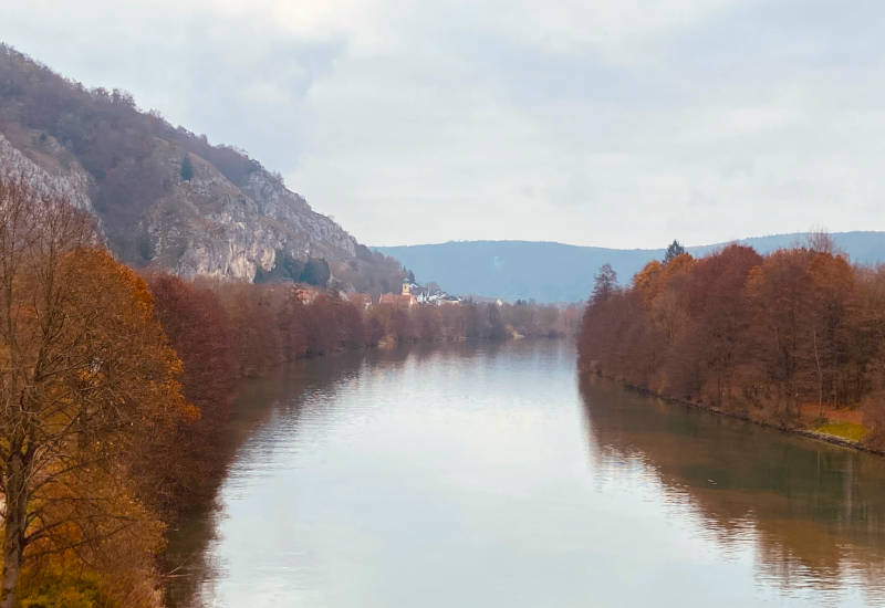 Herbstliche Landschaft mit Fluss und bewaldeten Hügeln.