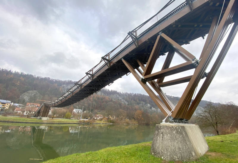Holzbrücke über einen Fluss mit bewaldetem Hintergrund.
