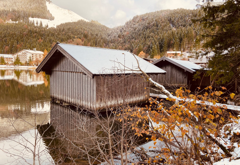 Holzhäuser am See, umgeben von Bergen und Bäumen.